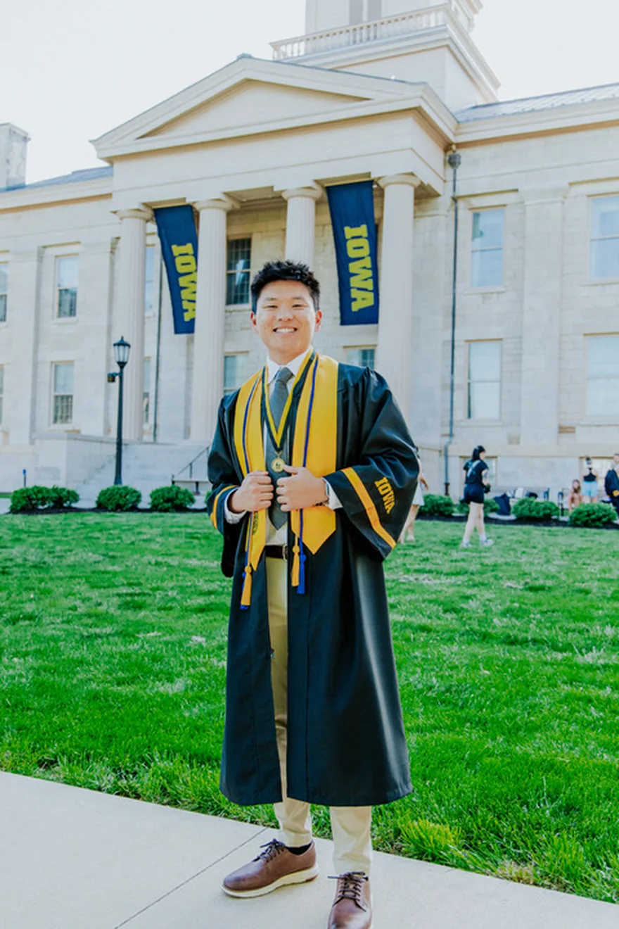 Nate Herkelman in cap and gown outside the Old Capitol at the University of Iowa.